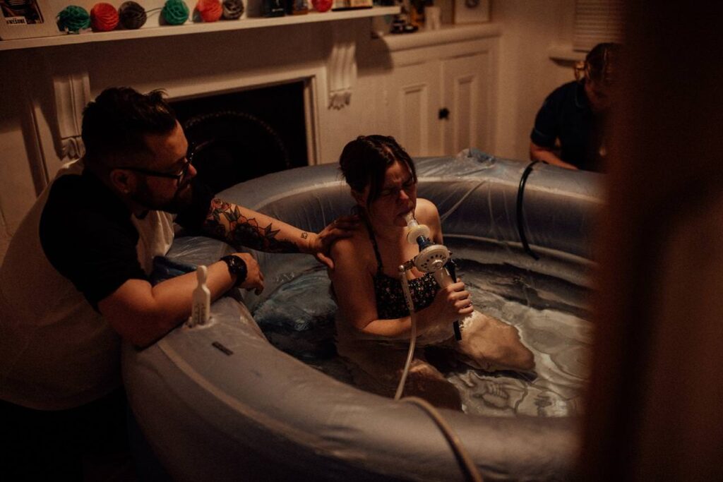 Partner offering reassurance during a home water birth, captured in a documentary photography style.