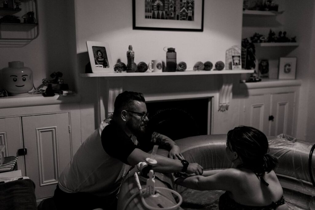 Mother labouring in a birthing pool at home holding hands with her partner