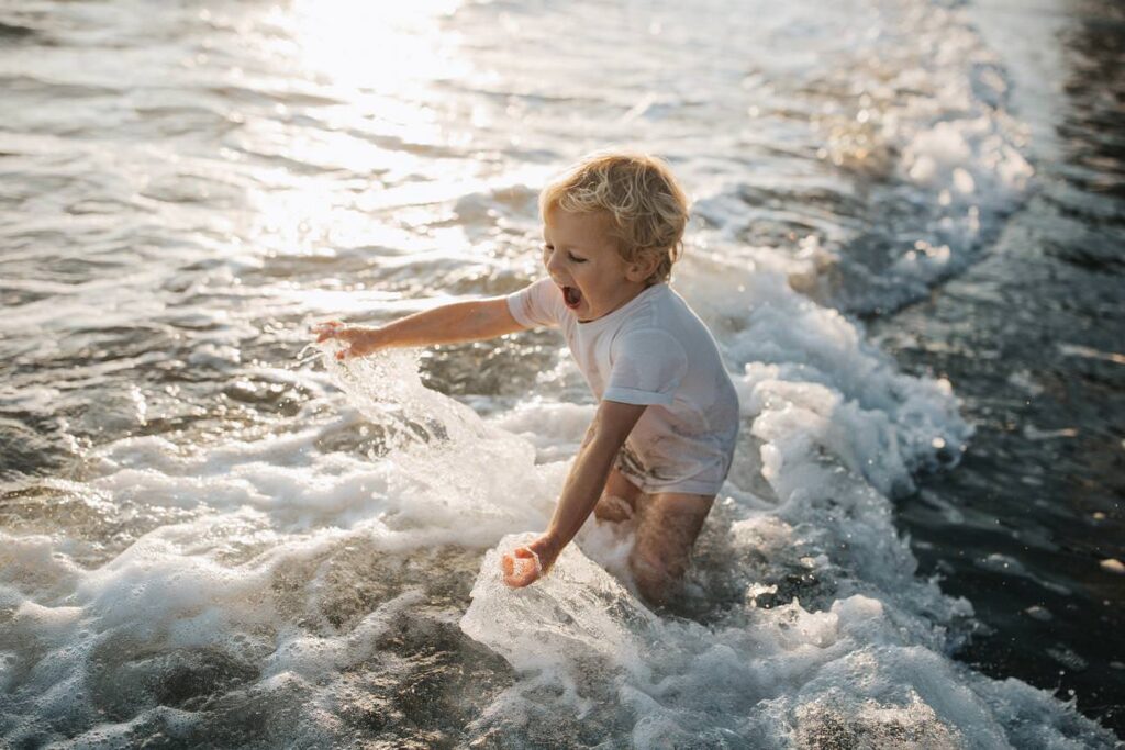 little boy playing in the sea during family photography session at tregantle beach cornwall
