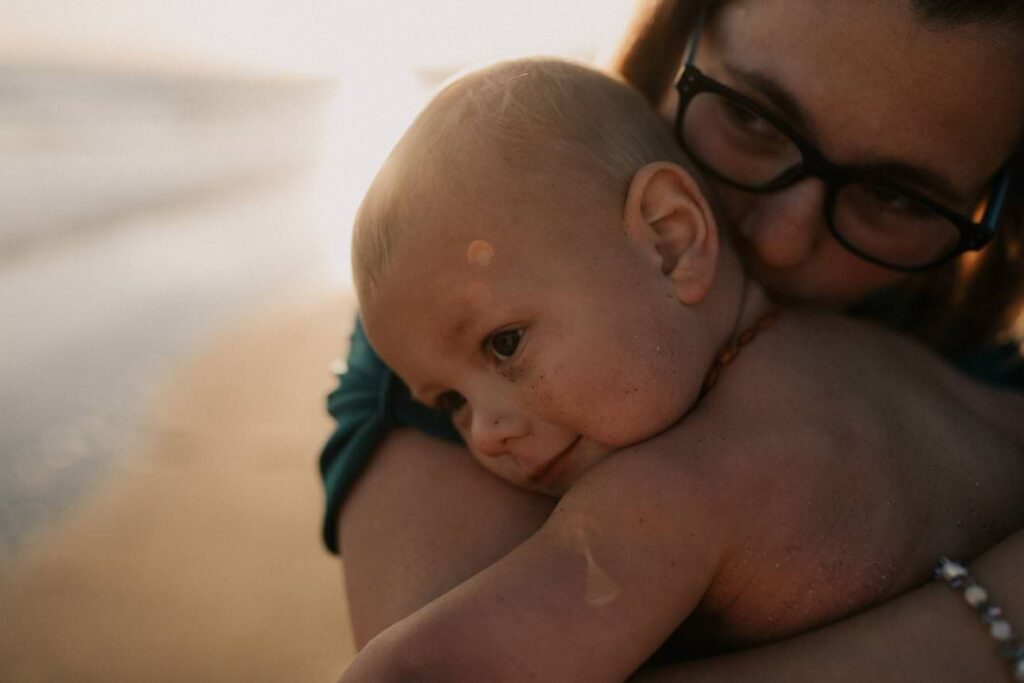 mother cuddling her baby on the beach at sunset