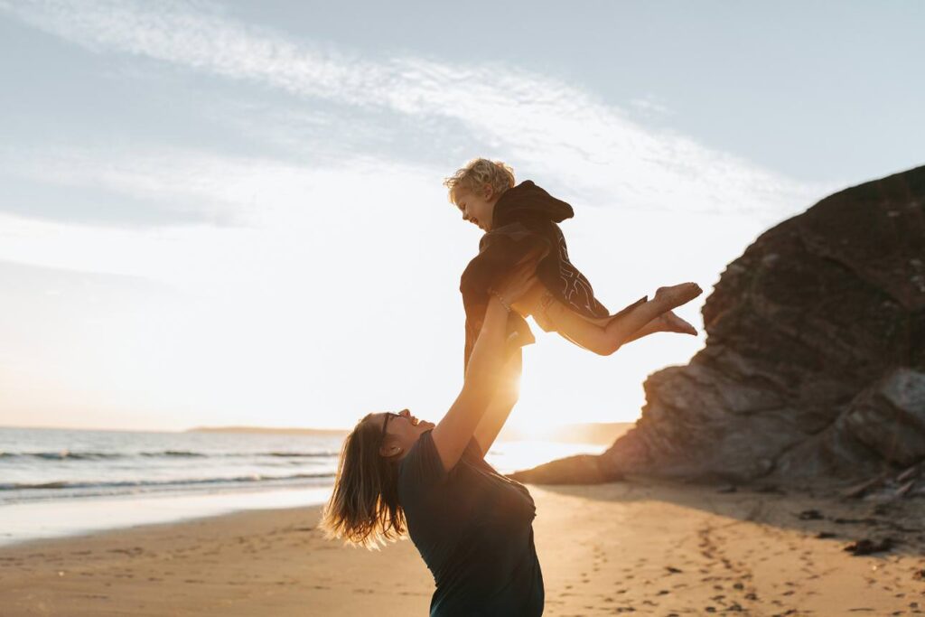 mother holding her son in the air at sunset in cornwall