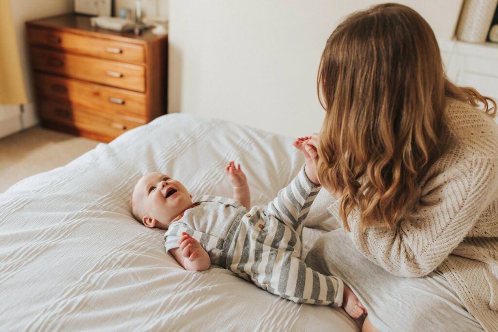 mother tickling her baby's feet while he lays on the bed giggling during a motherhood photography session in plymouth
