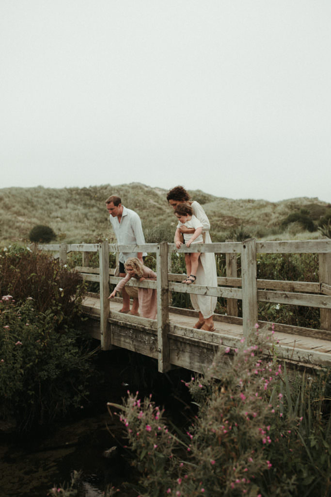 family of four looking over a bridge at the beach during lifestyle family photography session