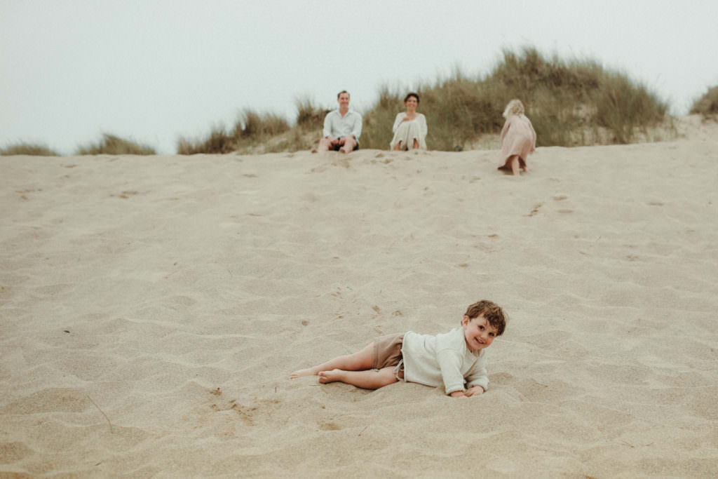 little boy rolls down the sand dunes during lifestyle family photography session