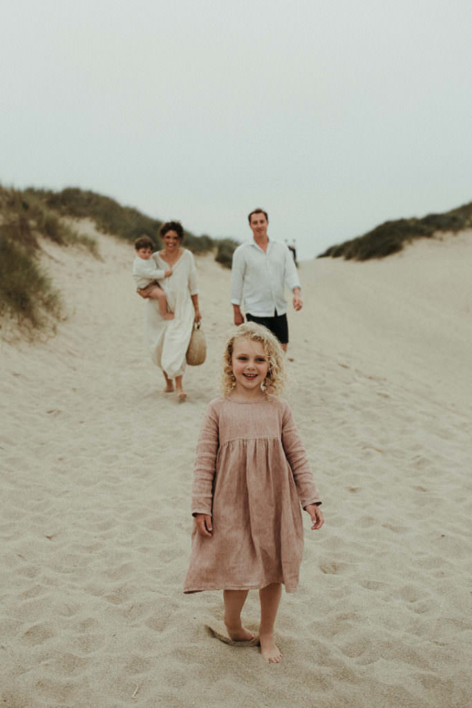 family walk towards camera with little girl in foreground at the beach during lifestyle family photography session