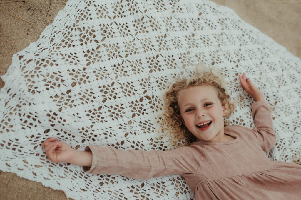 overhead shot of little girl playing on blanket on the beach during ifestyle family photography session