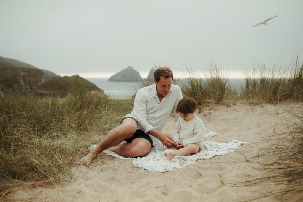Father and son sit on blanket in the sand dunes during lifestyle family photography session