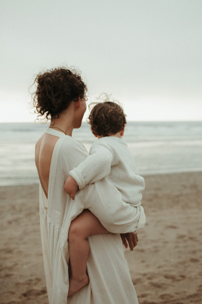 back shot of mother holding toddler and looking out to sea during lifestyle family photography session