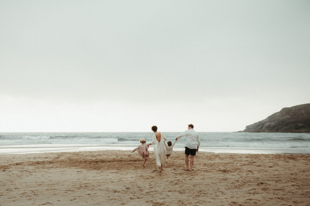 family of four swing children as they walk towards the sea during lifestyle family photography