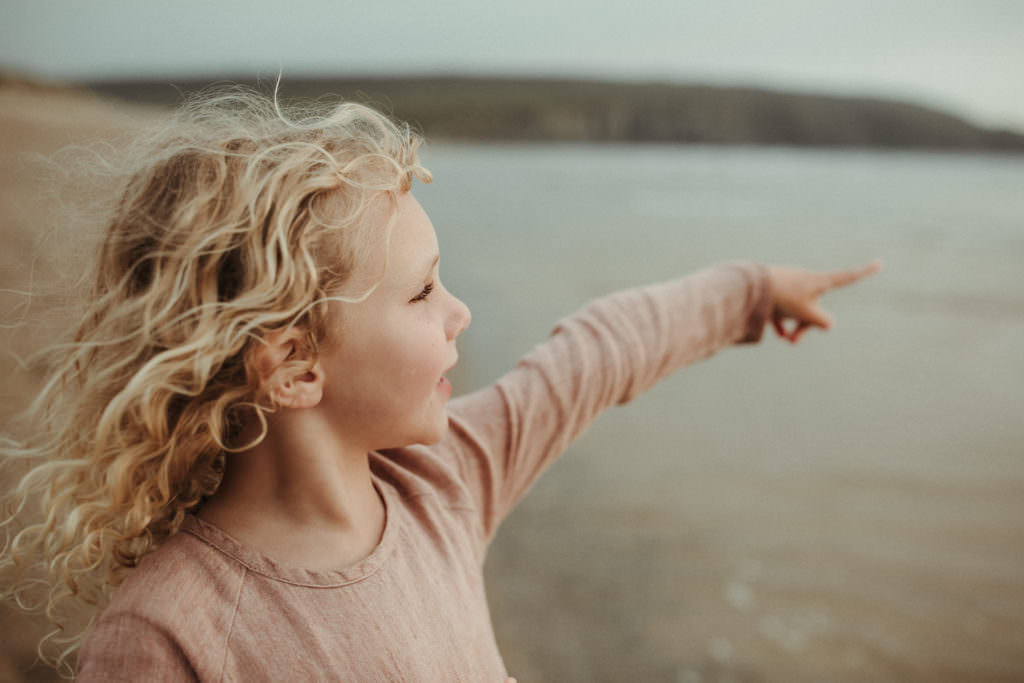blonde curly haired girl points out to sea during lifestyle family photography session