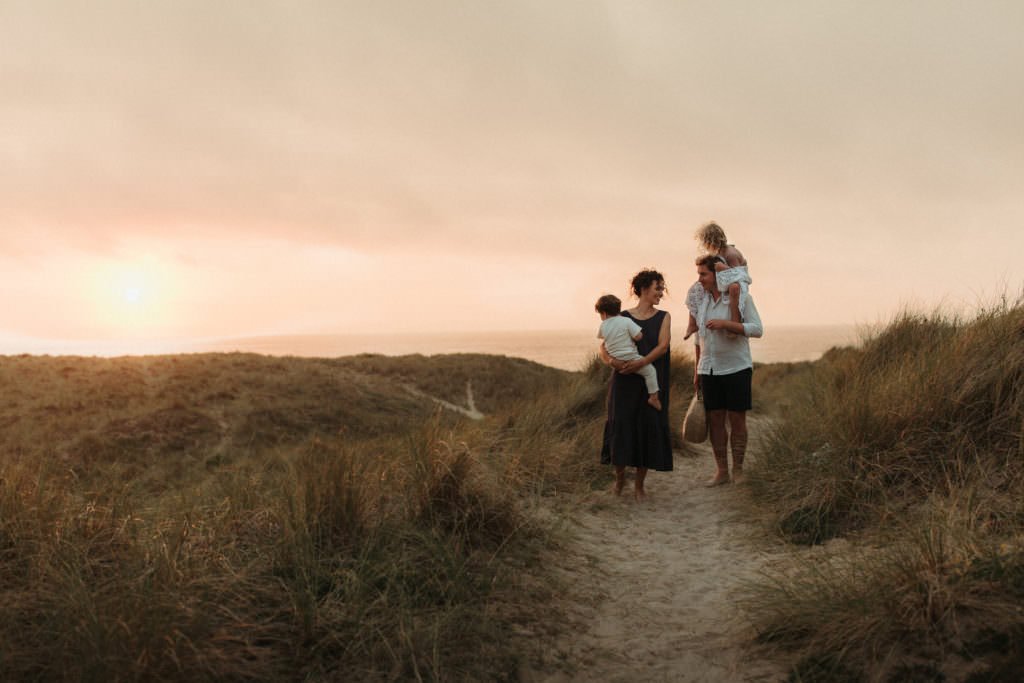lifestyle family photography family walking away from beach with beautiful pink sunset sky