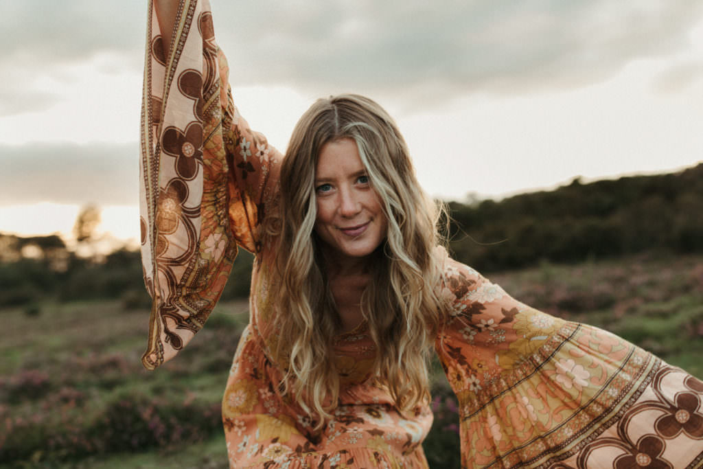 family photographer devon shoot Woman leans into camera with arms up wearing orange spell and gypsy dress