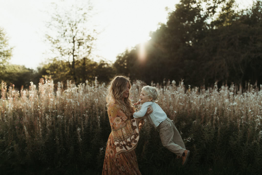 family photographer devon shoot Mum swings little boy in front of wild grasses