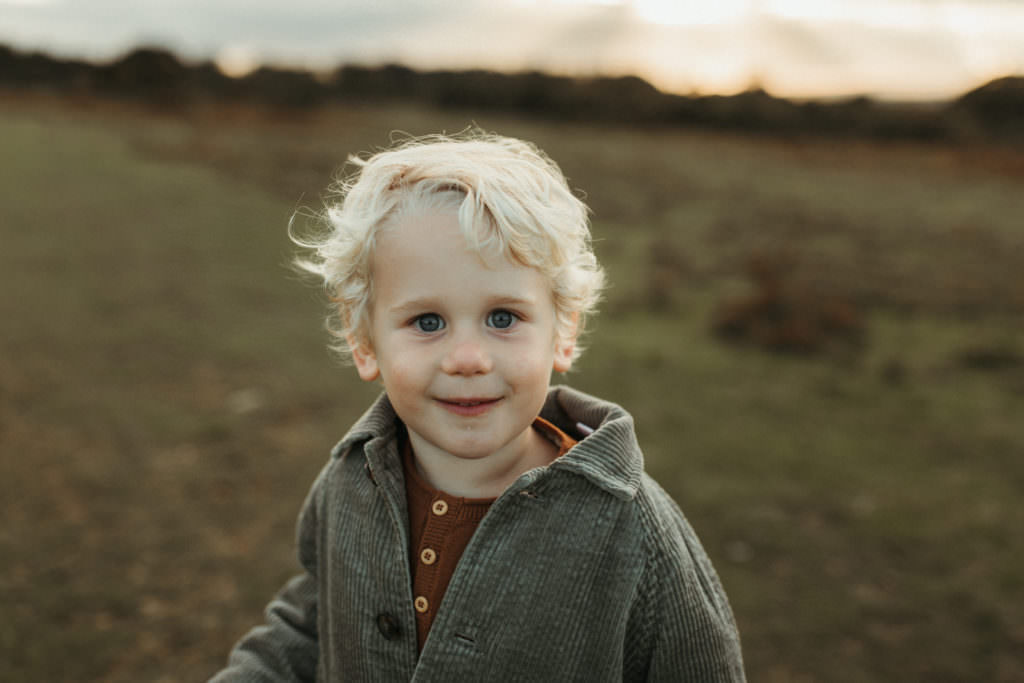 family photographer devon shoot Little blonde boy smiles into camera with beautiful light highlighting him