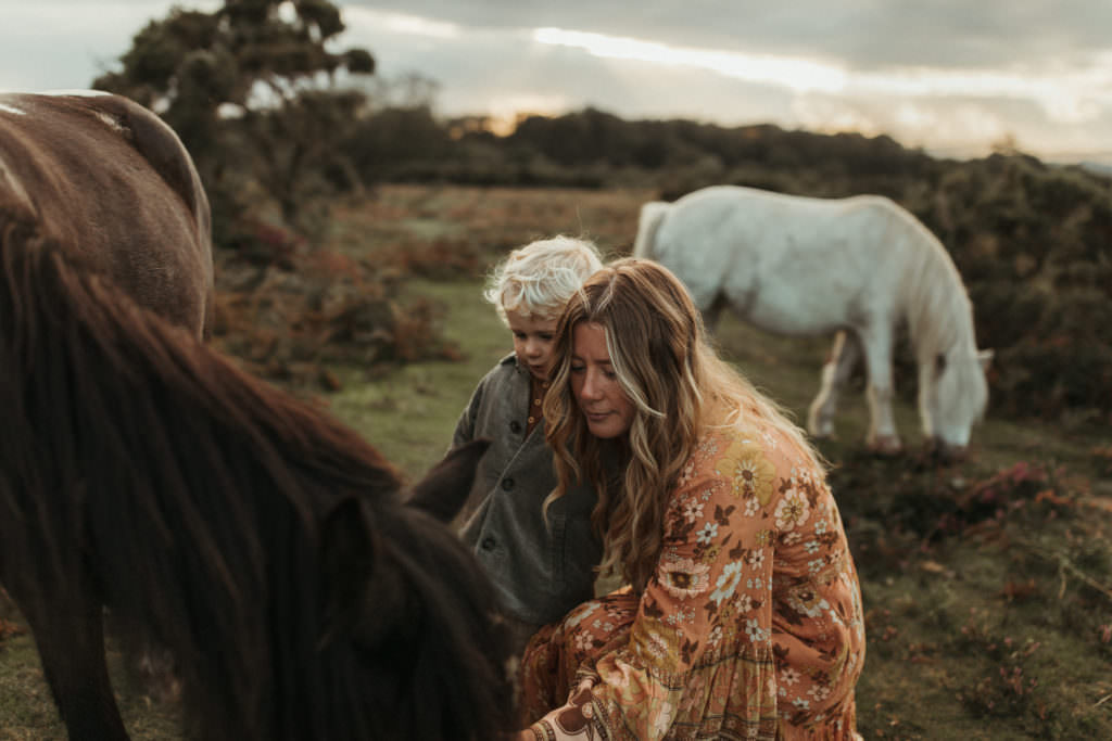 family photographer devon shoot Mum and son leaning down and stroking brown wild horse