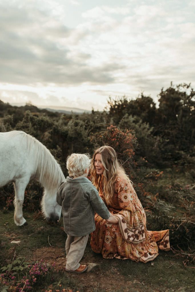 family photographer devon shoot Mum hold hand of son encouraging him to stroke wild white horse