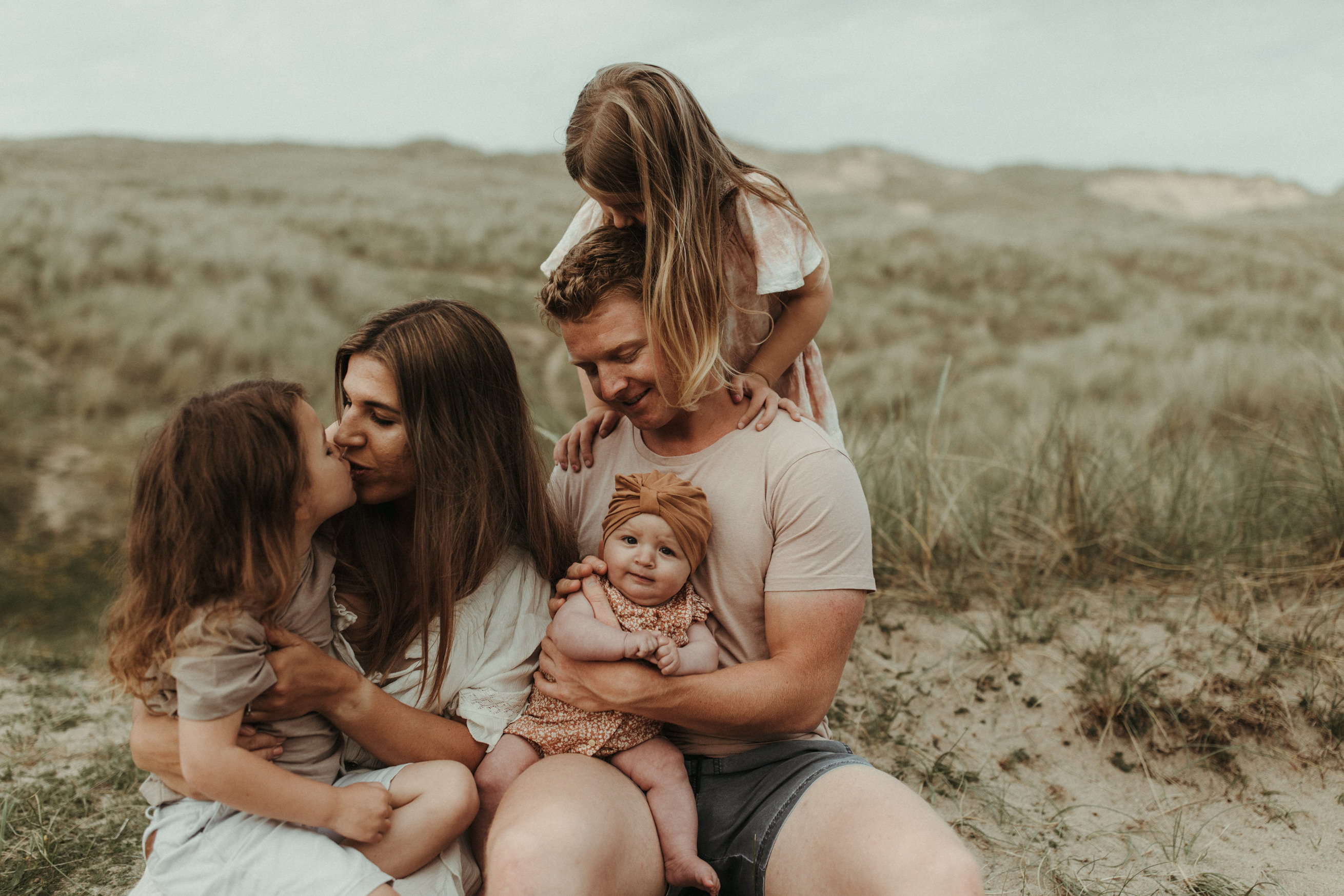 Family of 5 in muted tones sit on beach for boho family photos