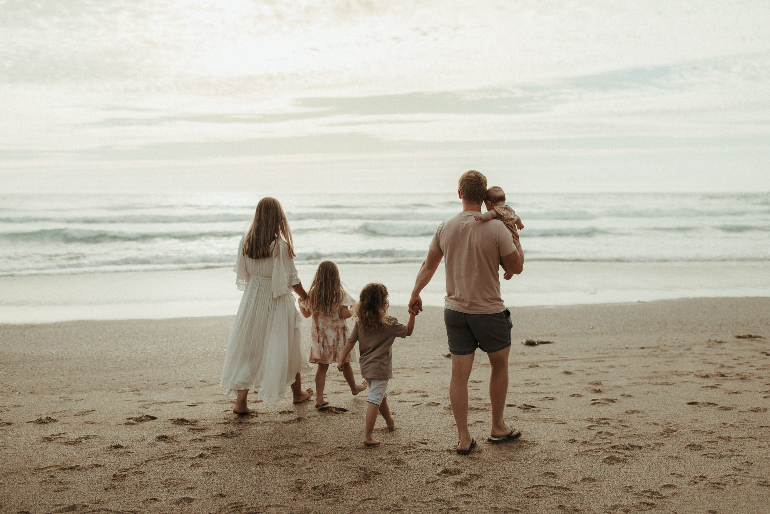 Family of 5 hold hands and walk towards sea boho family photos