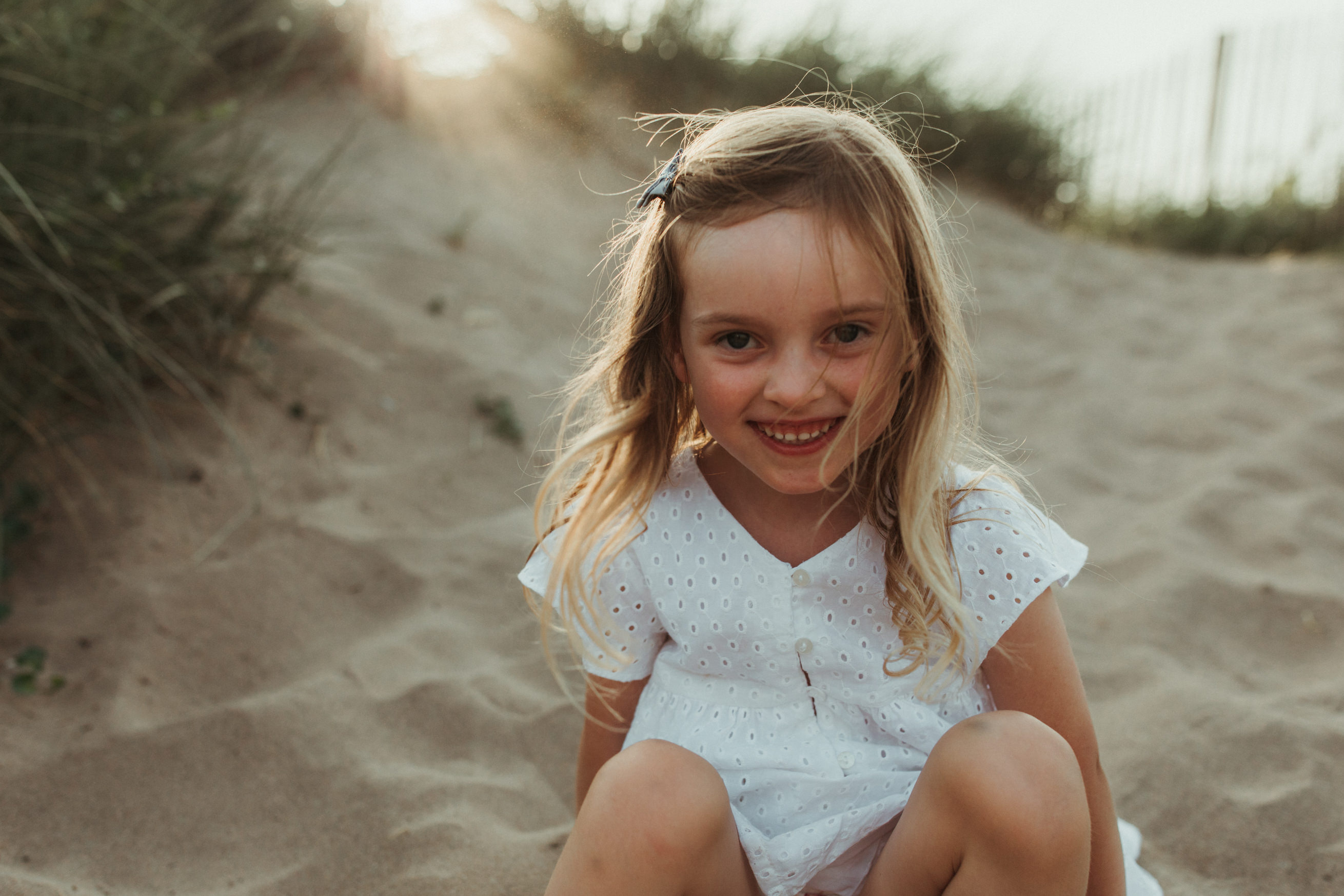 little girl smiles at the camera on the beach. How do I make my children behave for photographs?