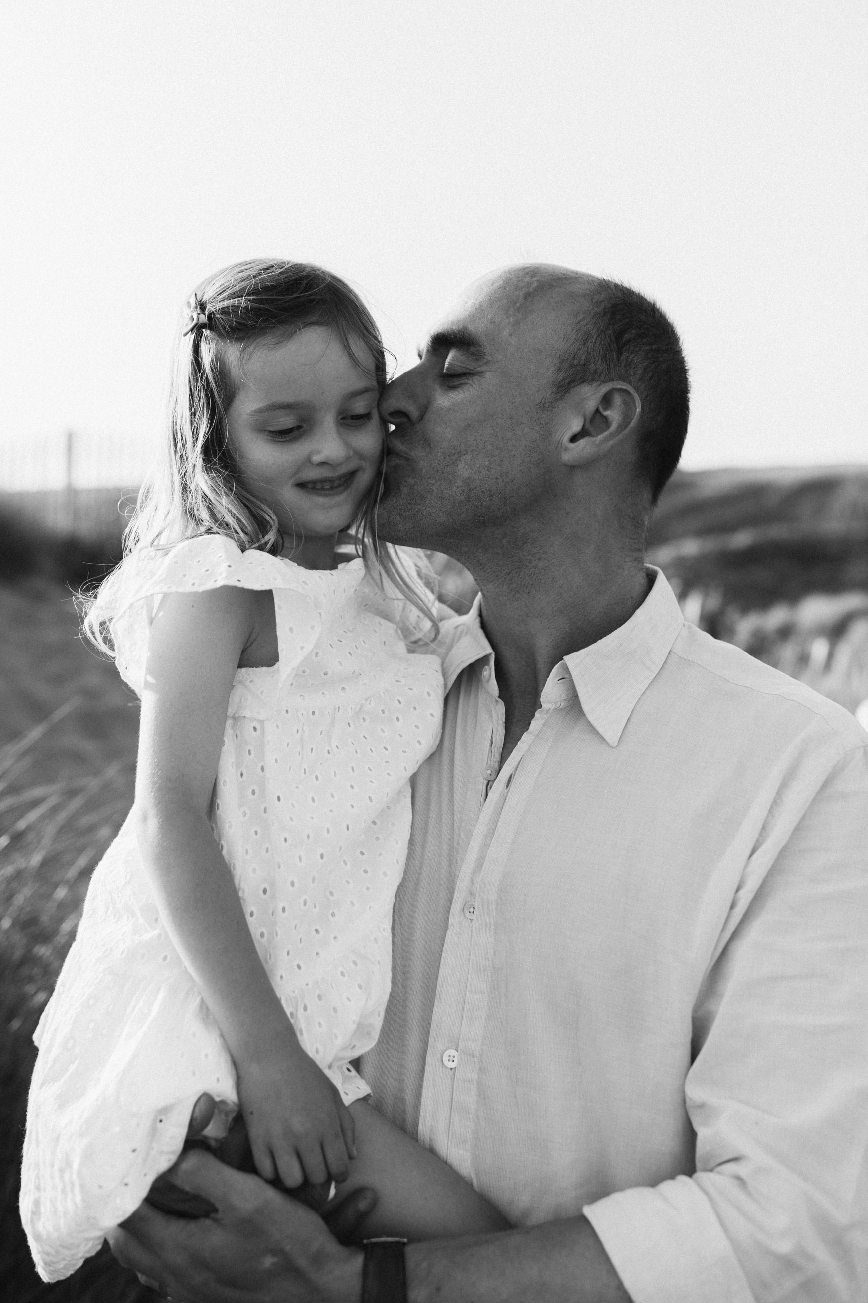 Dad hols little girl and kisses her cheek