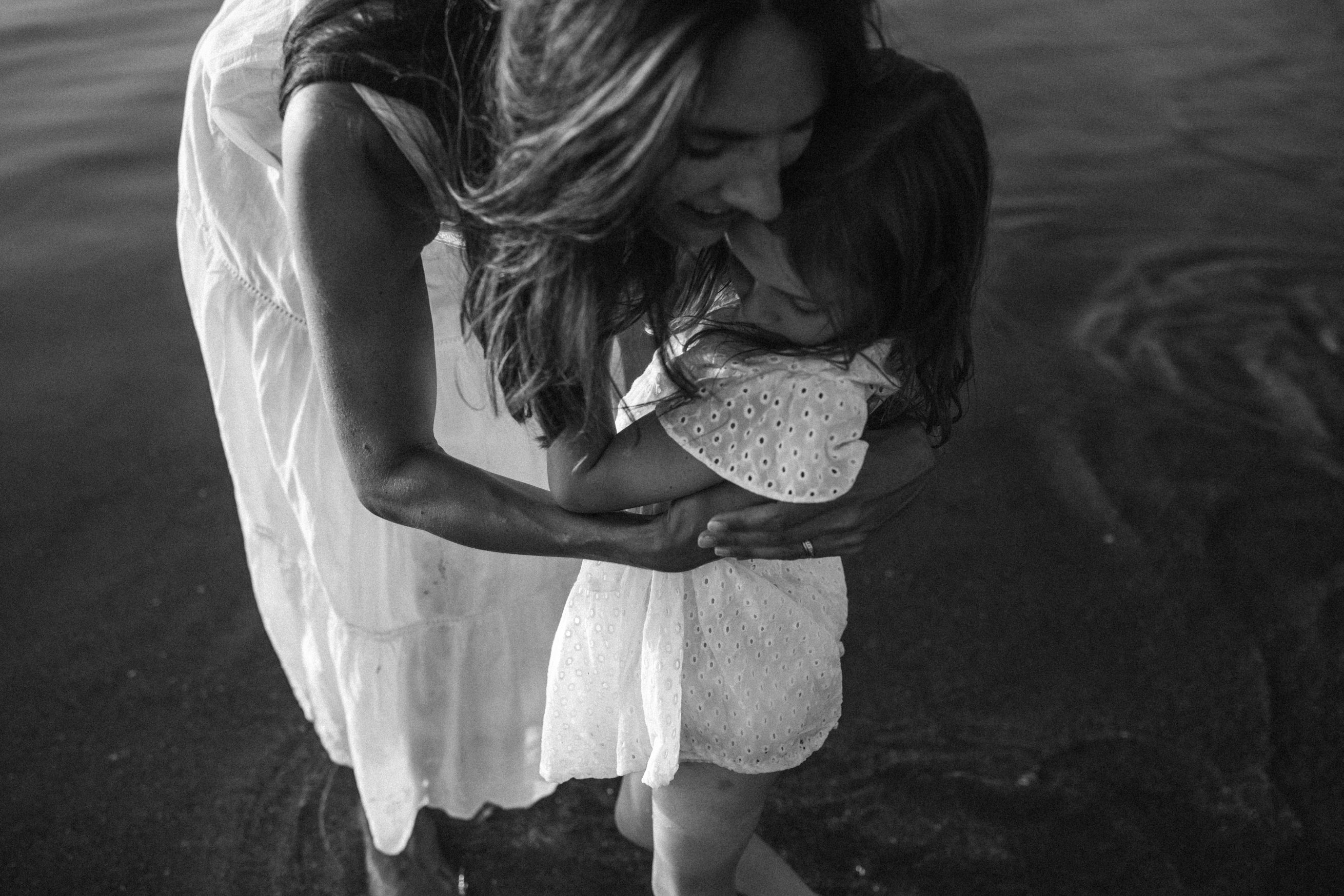 Mother leans down and hugs little girl in the sea