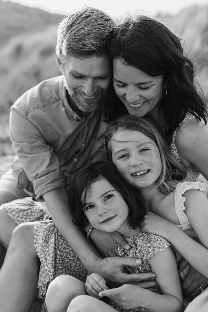 Black and white image of parents with their children cuddled up together and smiling during their session with Melanie Grace Cornwall family photographer.