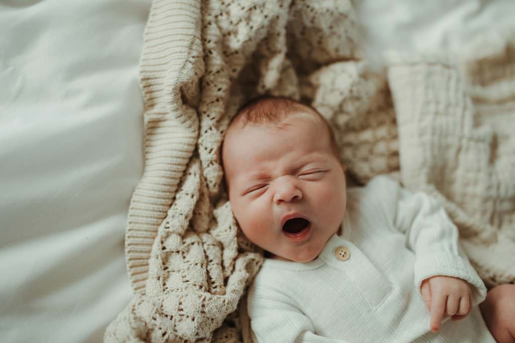 Close up of baby laying on a bed on a beige blanket yawning. Wadebridge Newborn Photographer