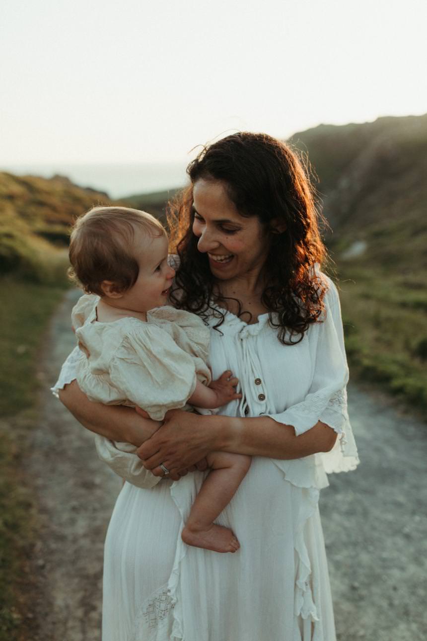 Mother holding her toddler and smiling during their family photography session in Cornwall