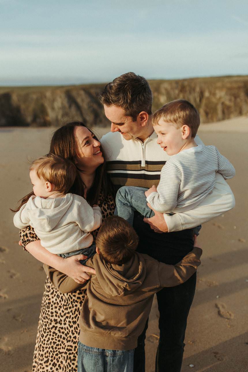 A family hugging each other at stood on the beach at sunset, taken by Melanie Grace Cornwall Family Photographer