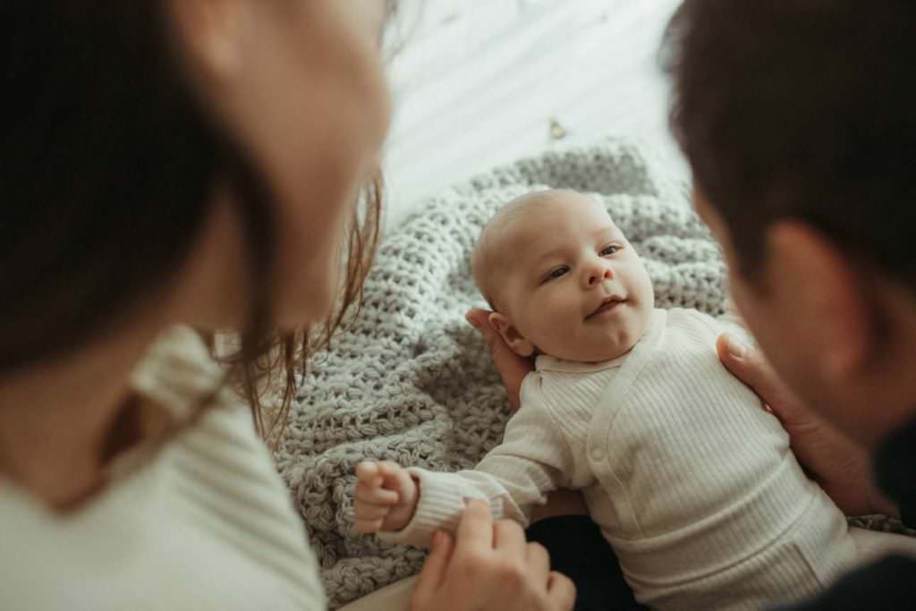 Mother and father looking down at their baby who's laying on the bed looking up at them in their home in Cornwall.