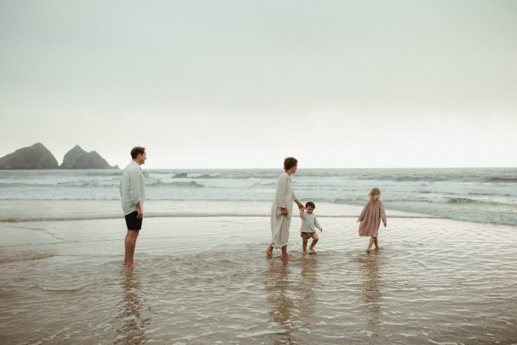 family walking in the sea on a beach in Cornwall as the sun is setting.