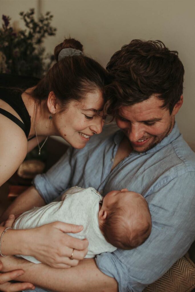 mother and father holding newborn baby in soft morning light
