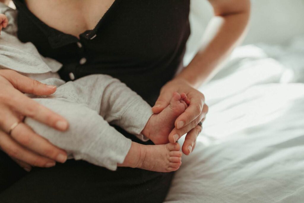 Mother holding newborn baby’s tiny toes in soft natural light at home in Cornwall