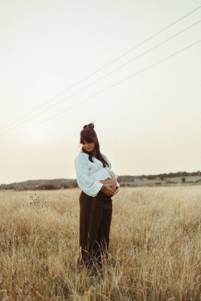 natural maternity portrait of woman standing in long grass during golden hour