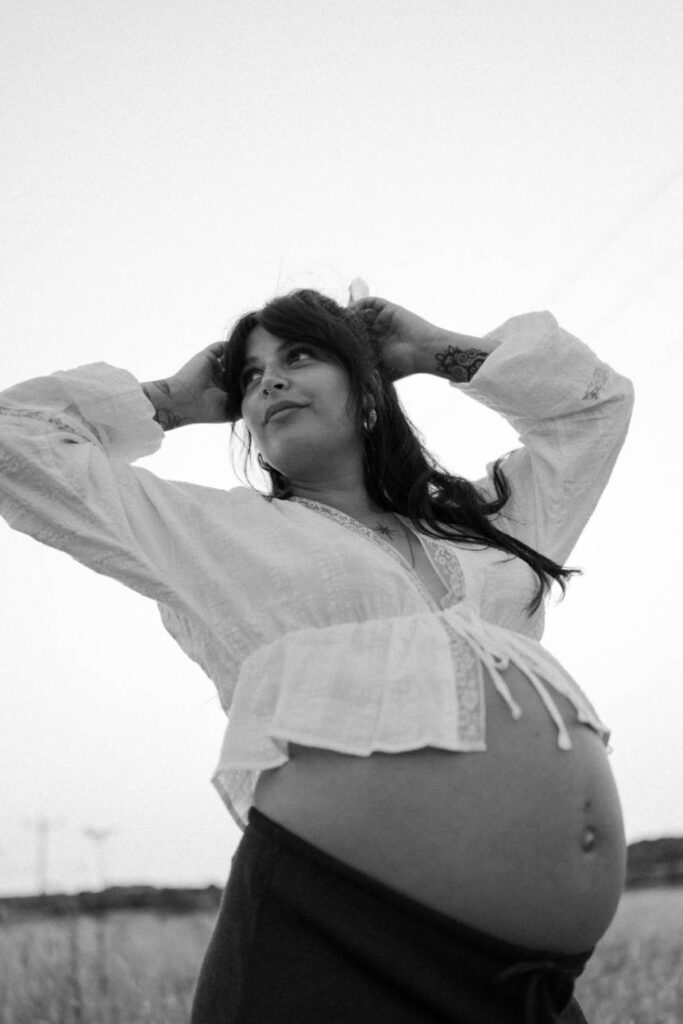 a natural maternity portrait of woman standing in long grass during golden hour