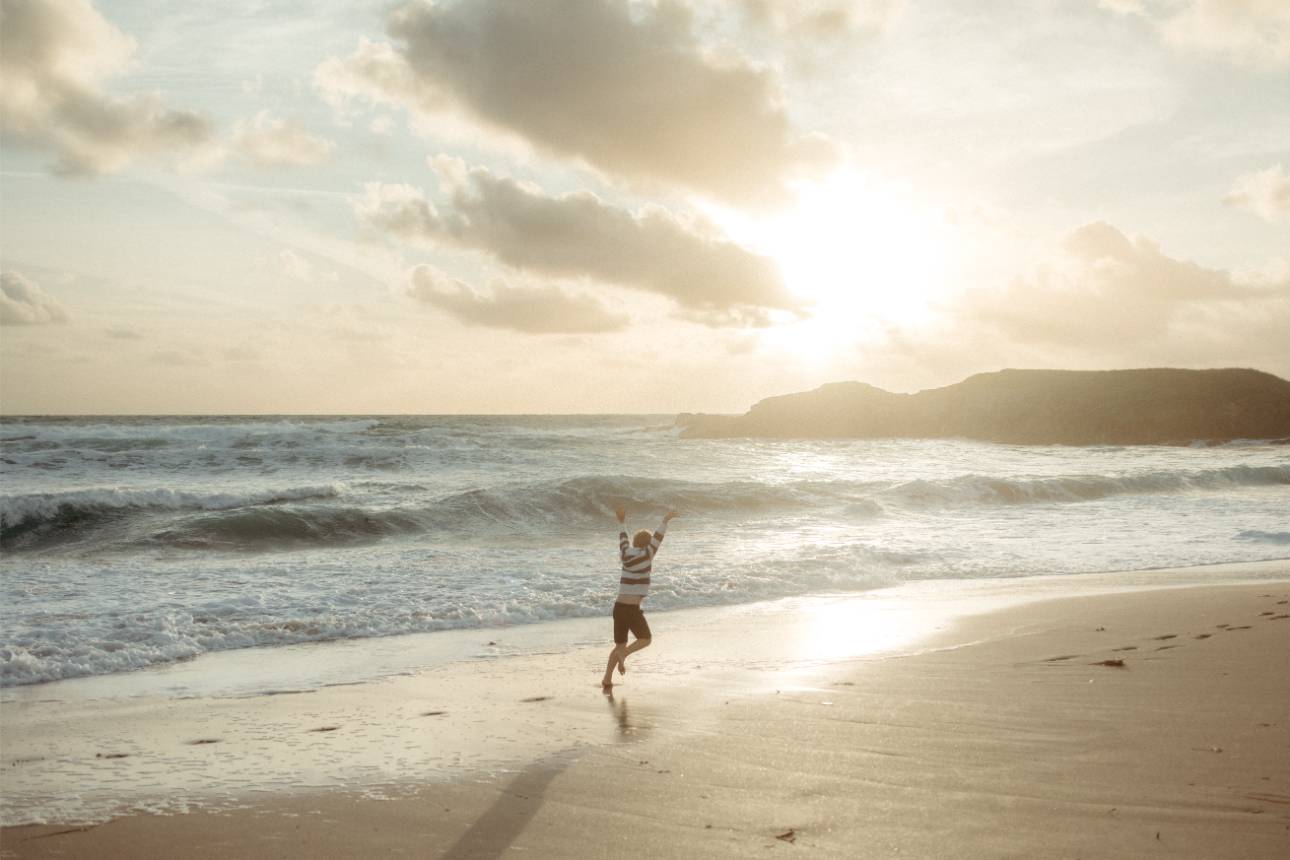 Boy running across the beach at sunset in Cornwall