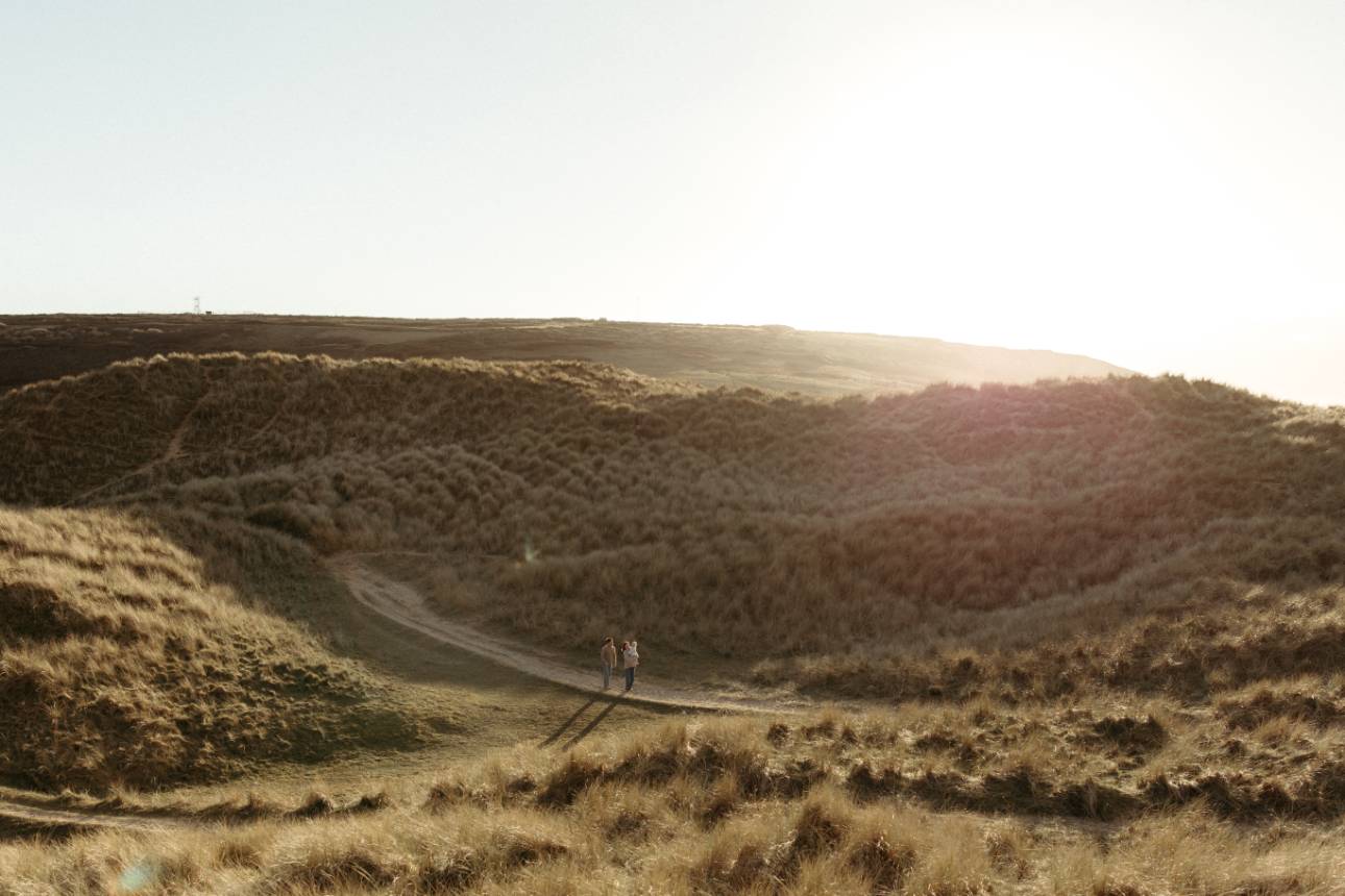 Family small in large landscape image of Cornwall beach sand dunes at sunset during relaxed family photoshoot.