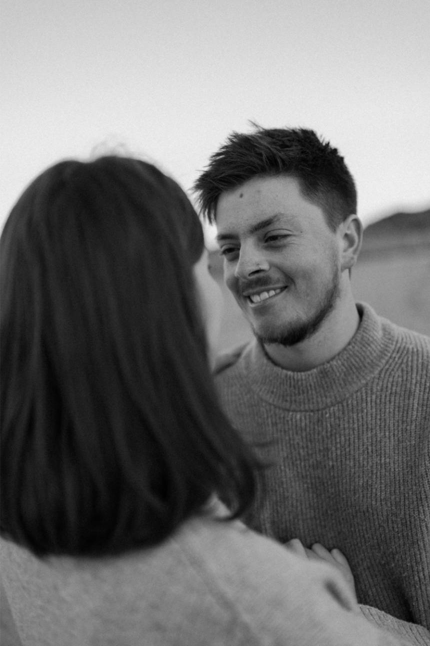 Husband gazing and smiling at wife during natural, relaxed Cornwall beach maternity photoshoot.
