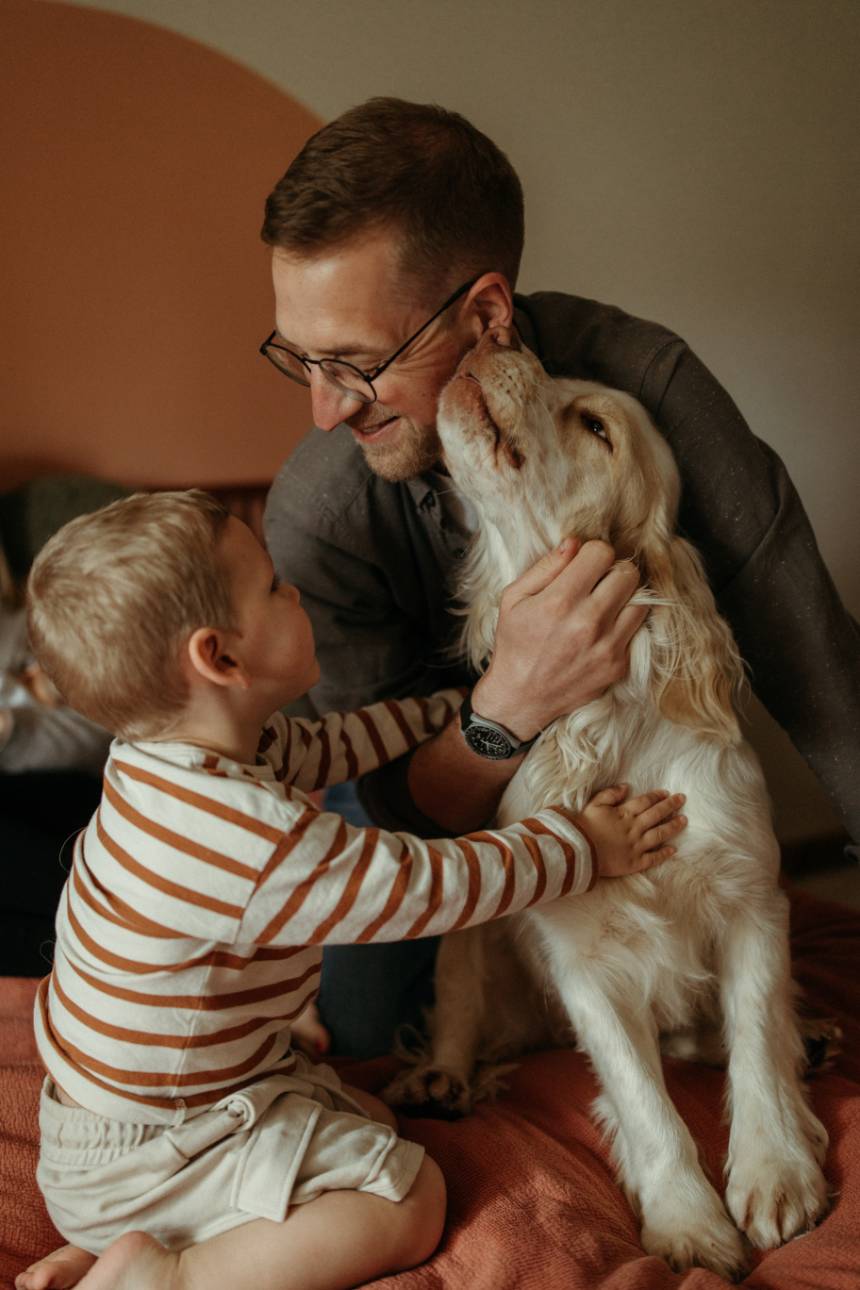 father and son cuddling pet dog during a natural newborn family photography session at home in Cornwall