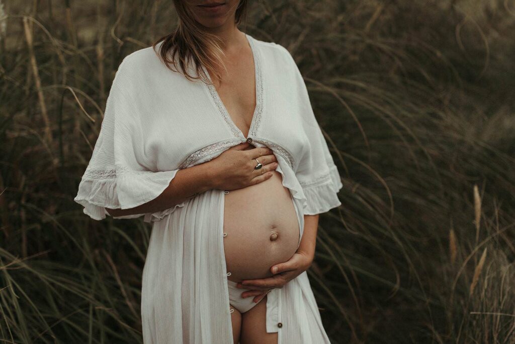 Expectant mother holding her bump surrounded by seagrass and pampas during her maternity photoshoot