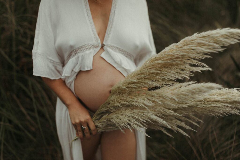 A mother holding bunches of pampas grass in-front of her baby bump