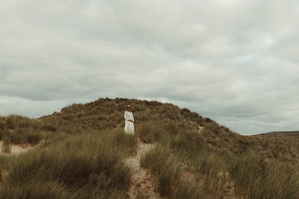 An expecting mother standing on the sand dunes in Cornwall