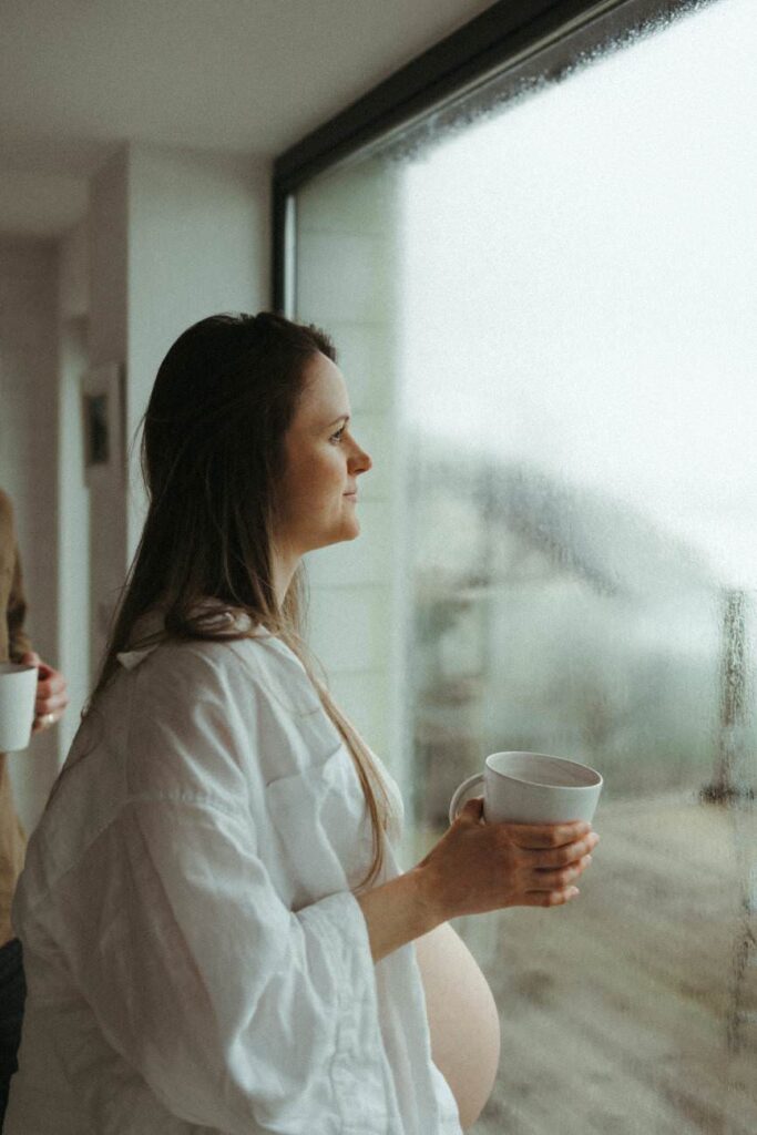 Pregnant mother gazing out to sea, coffee in hand