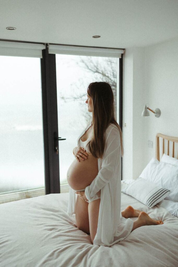 natural maternity portrait of a pregnant woman next to a window at home