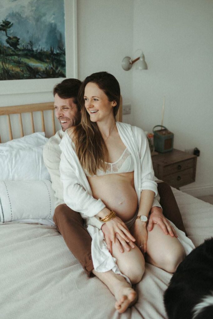 A couple laughing together during their in-home pregnancy photoshoot in Porthleven