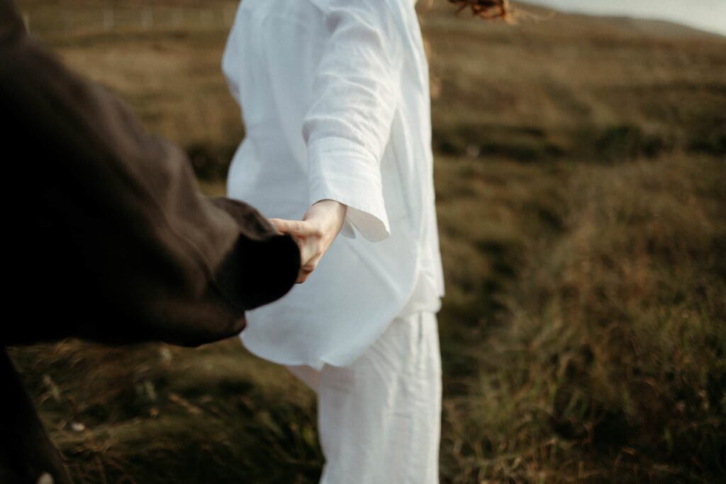 a couple holding hands wearing black and white during their relaxed maternity photography session in Cornwall