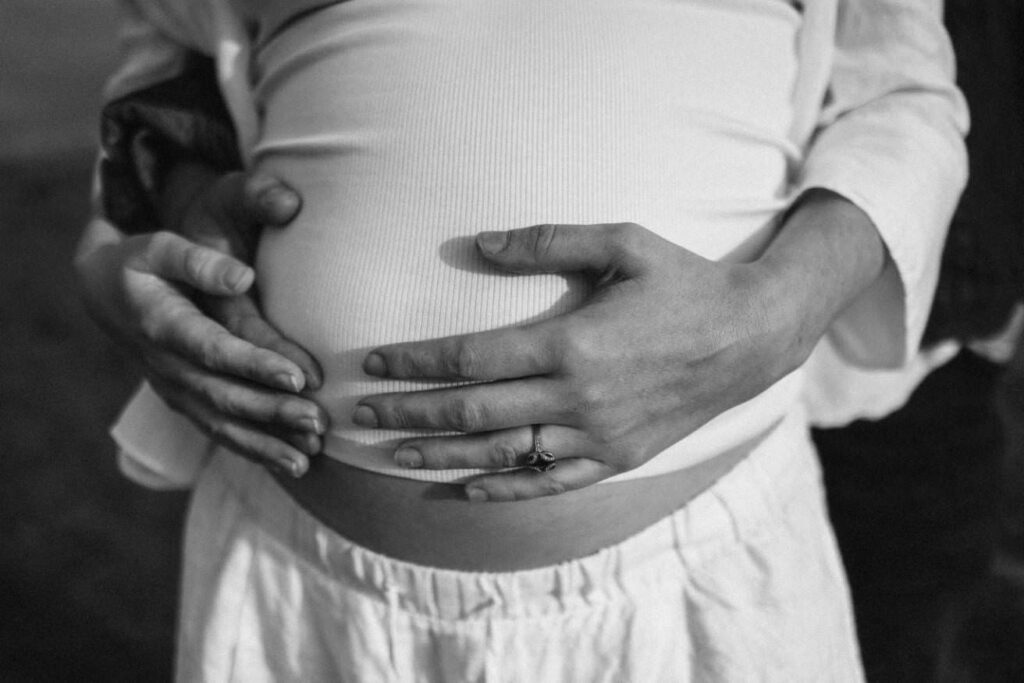 A close-up black and white image of a kothers hands resting on her baby bump during her maternity photoshoot.