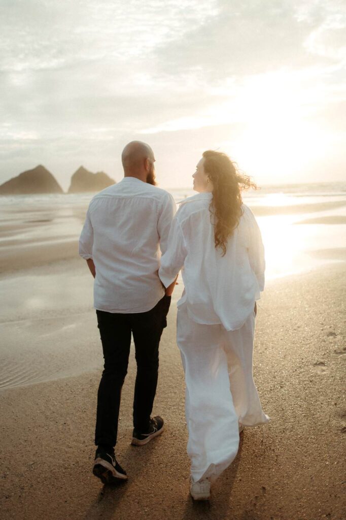 Couple walking along Cornish beach at sunset