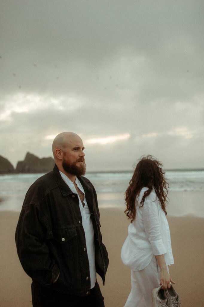 A couple walking across the beach together during their maternity photoshoot in Cornwall