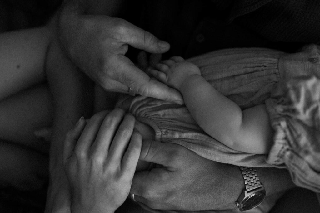 Close-up of parents hands holding baby during baby photoshoot at home in Cornwall